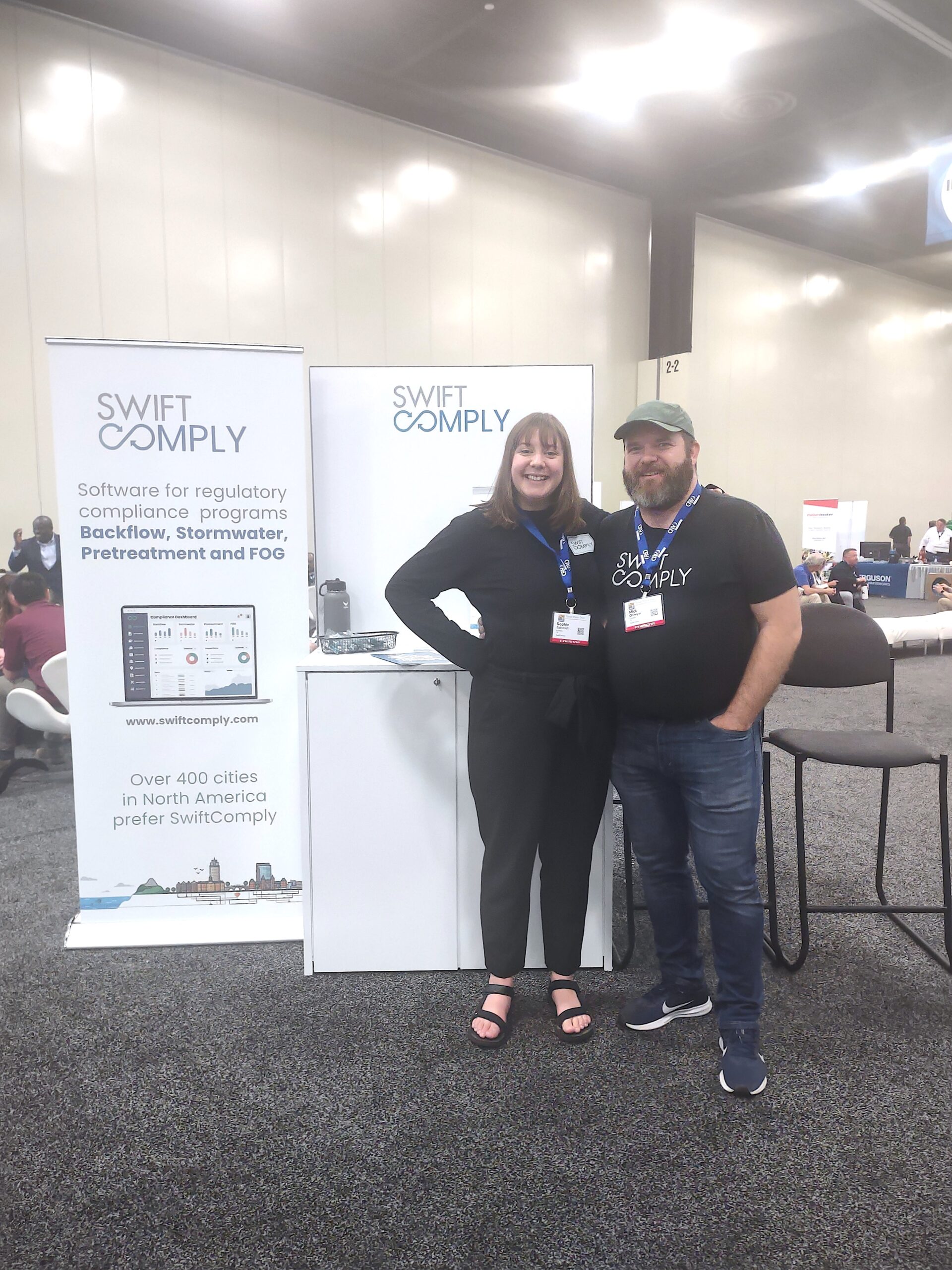 Mick and Sophie from SwiftComply in front of posters at a conference